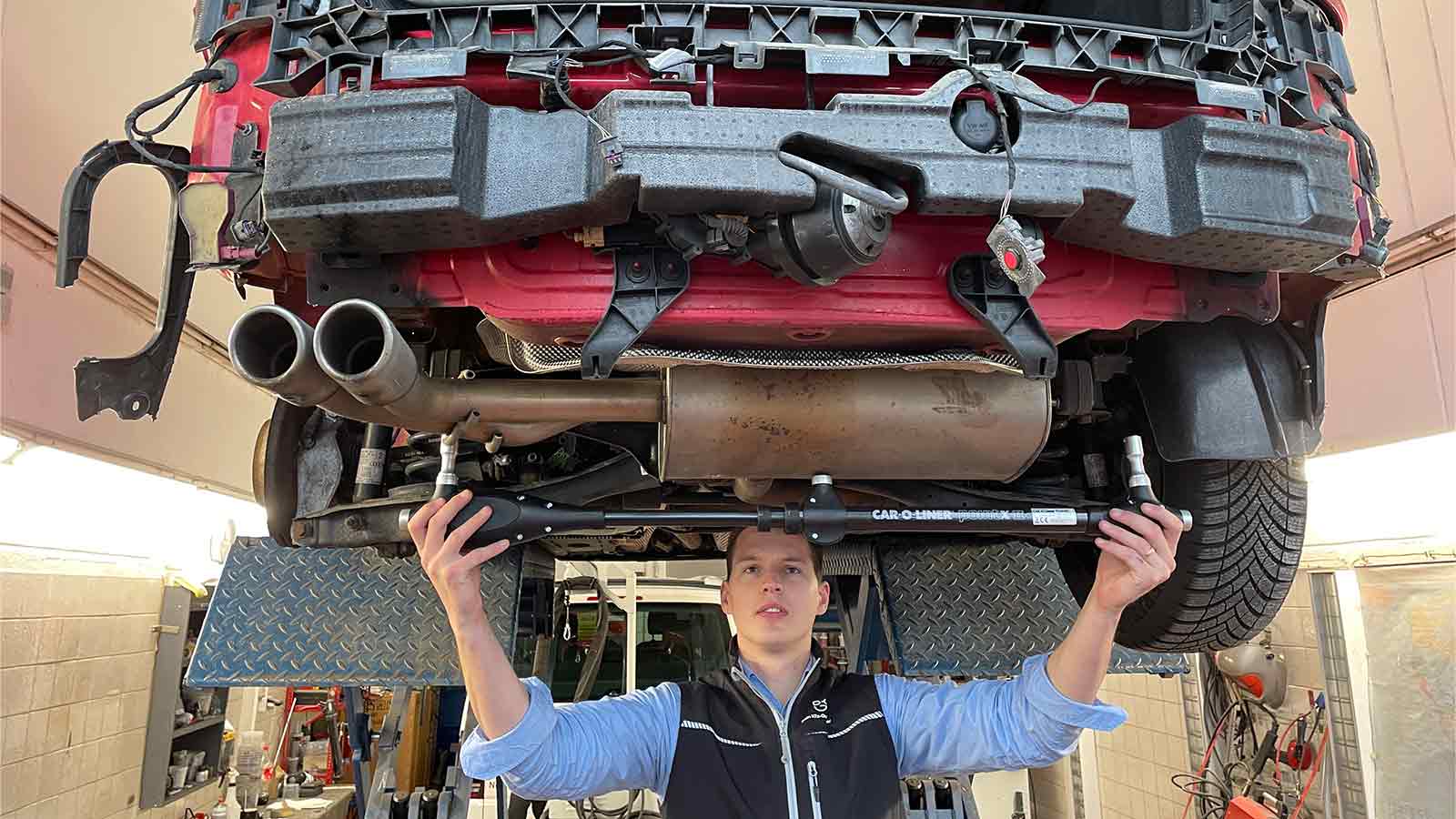 Sebastian Wyczisk hält unter der Hebebühne die Car-O-Liner-Messbrücke an den Unterboden eines roten Unfallautos